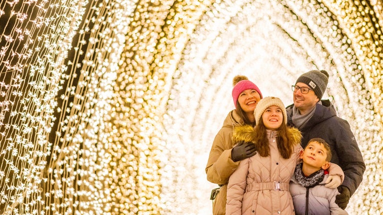 Two adults and two children stand in a cathedral-like archway of bright lights.